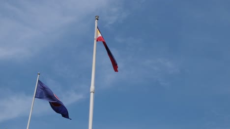 Philippine-National-Flag-and-the-ASEAN-Flag-flying-together-at-the-Philippine-Embassy-in-Bangkok,-Thailand-with-blue-lovely-sky-and-some-clouds
