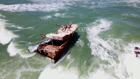 Drone-orbit-around-weathered-shipwreck-on-Cape-Agulhas-coastline,-Overberg