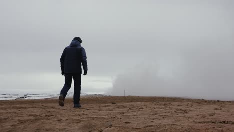 Tourist-walk-on-orange-volcanic-gravel-ground-toward-white-smoke-cloud