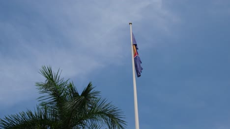 ASEAN-Flag-right-next-to-a-palm-tree-droops-down-on-a-pole-while-the-camera-slides-revealing-a-lovely-blue-sky-and-some-thin-white-clouds