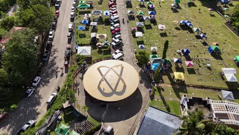 Aerial-drone-footage-of-Memorial-Park-in-Surigao-City---Philippines,-on-All-Souls-Day,-showing-cars-parked-and-gazebos-on-a-field-surrounded-by-lush-greenery