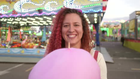 happy-woman-smiles-at-camera-with-cotton-candy-and-fair-background