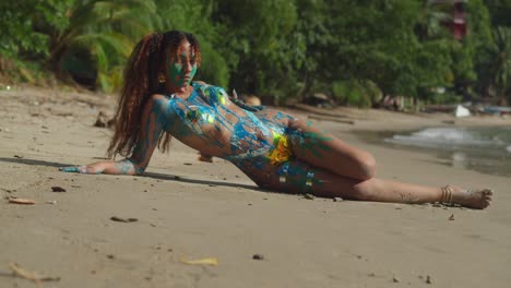 Sexy-girl-in-body-paint-laying-on-the-sand-with-ocean-waves-in-the-background-on-a-tropical-island