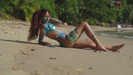 A-girl-in-body-paint-lays-in-the-golden-brown-sand-of-a-beach-on-a-Caribbean-island