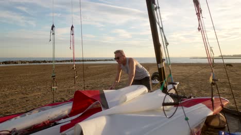 Hombre-Preparando-Las-Velas-De-Un-Catamarán-En-La-Playa-Por-La-Mañana.