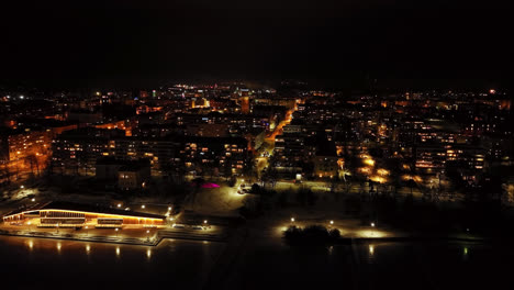 Drone-shot-ascending-in-front-of-the-night-lit-Vaasa-city,-in-Osterbotten,-Finland