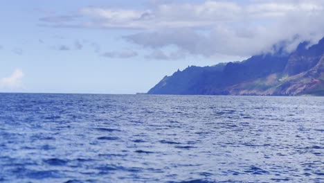 Filmischer-Schwenk-Mit-Langer-Linse-Von-Einem-Boot-Aus-An-Der-Wunderschönen-Küste-Von-Na-Pali-Mit-Spinnerdelfinen,-Die-Aus-Dem-Meer-In-Kaua&#39;i,-Hawaii,-Springen