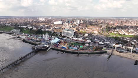 Adventure-Island-and-Southend-Pier-from-the-air,-wide-drone-sweep-show-the-whole-theme-park-site,-section-of-the-famous-pier-and-the-tower-blocks-and-town-beyond