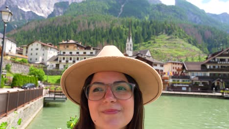 Close-up-of-woman-face-with-hat-enjoying-Lago-di-Alleghe,-village-in-background
