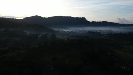 Ein-Nebliger-Sonnenaufgang-Im-Osten-Von-Bali-Mit-Dschungelgrün-Und-Bergsilhouetten,-Luftaufnahme