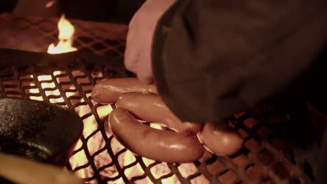Sausages-on-hot-metal-grill-over-night-camp-fire-are-flipped-by-hand