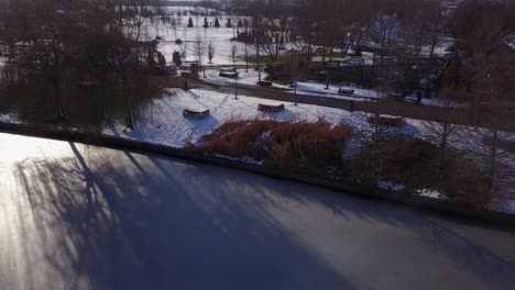 Flying-upwards-above-a-perfect-frozen-lake-looking-towards-the-snowy-park-of-Mogosoaia,-Bucharest,-Romania