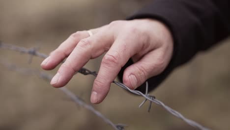 Mens-hand-slowly-moving-on-barbed-wire