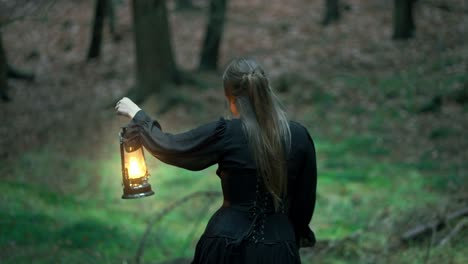 Girl-with-long-hair-and-a-black-dress-walks-through-a-dark-forest-with-a-lamp-in-her-hand