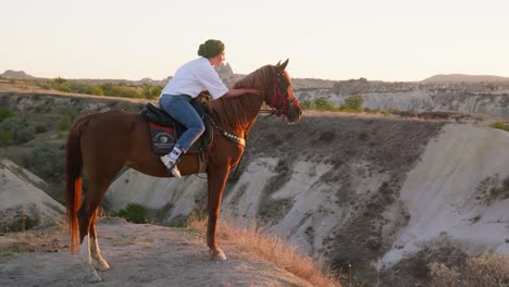 Female-sunset-rider-calms-horse-valley-overlook-landscape-golden-hour