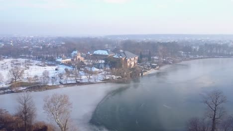 Flying-above-a-frozen-lake-towards-the-Brancoveanu-Palace-of-Mogosoaia,-Bucharest,-Romania