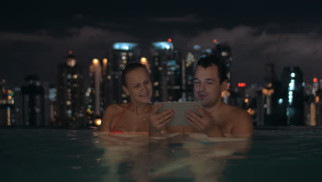 Couple-with-touch-pad-in-rooftop-pool-at-night
