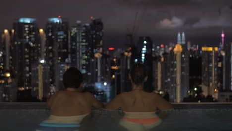 Im-Pool-Auf-Dem-Dach-Eines-Hotels-In-Kuala-Lumpur,-Malaysia-Mann-Und-Frau-Blicken-Auf-Die-Nächtliche-Stadt