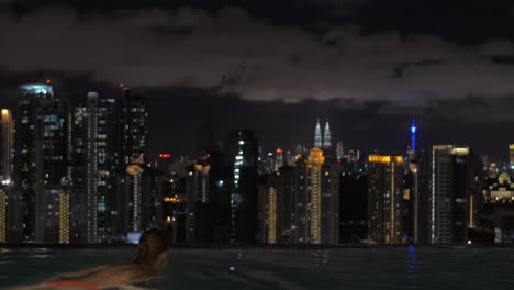 Woman-looking-at-night-Kuala-Lumpur-from-rooftop-pool