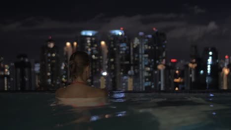 View-of-woman-in-the-pool-on-the-skyscraper-roof-and-then-swimming-man-about-her-on-night-city-landscape-Kuala-Lumpur-Malaysia