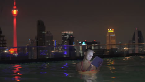 Im-Pool-Auf-Dem-Dach-Eines-Hotels-In-Kuala-Lumpur,-Malaysia-Schwimmt-Ein-Junges-Mädchen-Und-Arbeitet-An-Einem-Tablet
