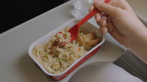 Close-up-clip-of-woman-eating-airplane-dinner-rise-with-vegetables-by-plastic-fork-against-window
