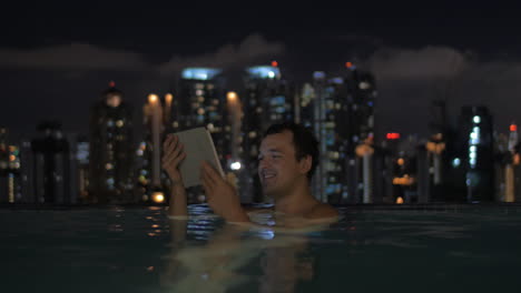 Man-with-pad-in-rooftop-pool-of-night-Kuala-Lumpur