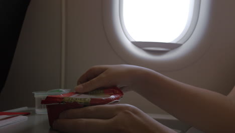 Close-up-clip-of-woman-eating-airplane-dinner-rise-with-vegetables-by-plastic-fork-against-window