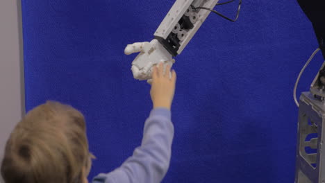 Close-up-view-of-boy-hand-holds-white-moving-plastic-hand-of-humanoid-robot-in-Robotics-exhibition-in-Moscow-Russia