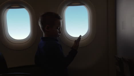 In-Der-Flugzeugkabine-Hält-Ein-Kleiner-Junge-Ein-Telefon-Und-Schaut-Sich-Ein-Video-An