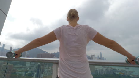 In-Hongkong,-China,-Macht-Ein-Junges-Mädchen-Auf-Der-Terrasse-Übungen-Mit-Hanteln-Und-Ausgebreiteten-Händen