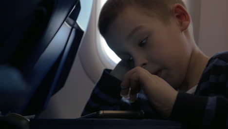 Im-Flugzeug-Sitzt-Ein-Kleiner-Junge-Und-Spielt-Spiele-Auf-Dem-Handy
