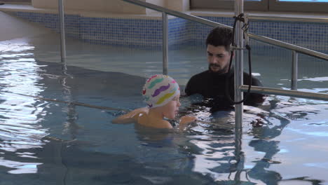 In-Der-Medizinischen-Klinik-Evexia-Im-Pool-Beobachtet-Ein-Arzt-Einen-Kleinen-Jungen,-Der-Schwimmt-Und-Ein-Geländer-Hält