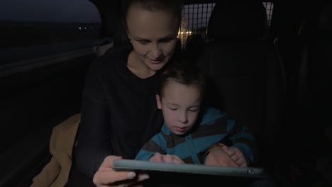 Mother-and-son-playing-with-touch-pad-during-night-car-ride