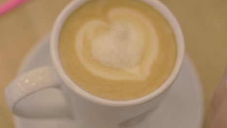 In-Eine-Tasse-Kaffee-Mit-Schaum-Gießt-Das-Mädchen-Zucker-Und-Rührt-Den-Kaffee-Mit-Einem-Löffel-Um