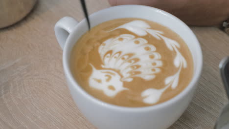 On-the-table-is-a-cup-of-coffee-with-foam-and-the-man-draws-on-the-foam-pattern