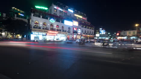 Zeitraffer-Der-Nächtlichen-Stadt-Quang-Truong-Dong-Kinh-Nghia-Thuc,-Gesehen-Einer-Stark-Befahrenen-Straße-Mit-Vorbeifahrenden-Autos,-Motorrädern-Und-Radfahrern,-Gebäuden-Mit-Werbeschildern