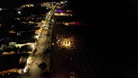 Beach-Bars-Aglow-with-Lights,-Waves-Gently-Lapping-the-Dark-Sea,-Evoking-Joyful-Summer-Vacation-Vibes-by-Night-in-Dhermi