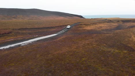SUV-car-driving-on-wet-gravel-road-in-nordic-landscape-toward-puddle