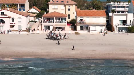 Aerial-tracking-shot-of-horseriders-galloping-along-the-Palavas-Beach-during-the-feria