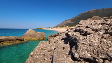 Hinter-Felsen-Lockt-Ein-Versteckter,-Geheimer-Strand,-Umspült-Vom-Azurblauen-Wasser-Des-Bezaubernden-Ionischen-Meeres-In-Albanien