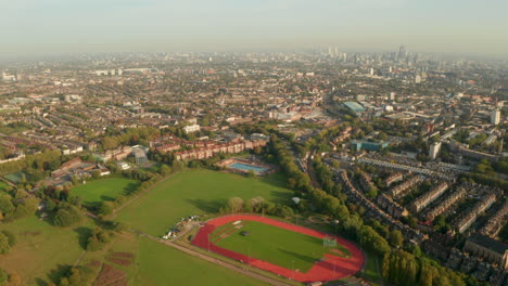 Descending-aerial-shot-of-sports-running-track-Hampstead-Heath-with-London-skyline-in-the-background