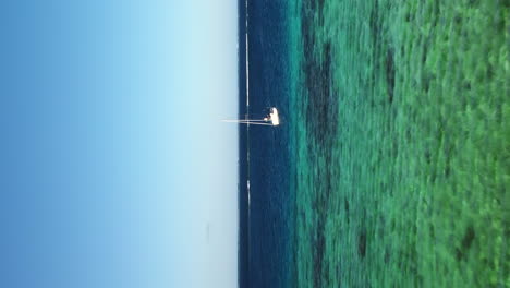 Sailboat-in-the-crystal-clear-waters-of-New-Caledonia---vertical-aerial