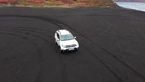 White-SUV-driving-on-black-sand-beach-on-atlantic-coast,-Iceland
