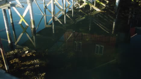 Reflections-in-water-of-fishing-cabin-and-walkway-over-ocean,-mid-shot