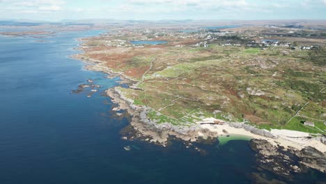 Wide-aerial-Coral-Beach-in-Ballyconneely,-clear-ocean-waters-and-rural-development-in-the-distance
