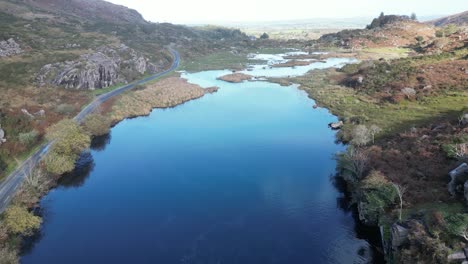 Revealing-drone-shot-of-the-Gap-of-Dunloe-Ireland-and-the-river-Loe,-with-a-road-on-the-shore