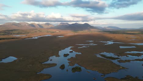 Wide-aerial-shot-of-Connemara-Lakes-with-calm-lakes-in-the-foreground-and-Beanna-Beola-mountain-range-in-the-distance,-slowly-rotating-drone-shot