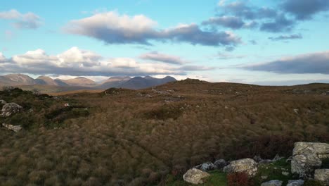 Drone-shot-of-Connemara-Lakes-with-rocks-and-calm-lakes-in-the-foreground-and-Beanna-Beola-mountain-range-in-the-distance,-taking-off-aerial-shot