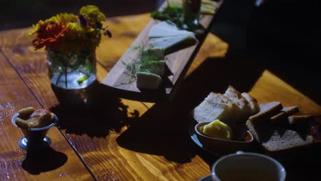 Cheese-board-being-placed-onto-table-of-food-with-bread-and-food,-mid-shot